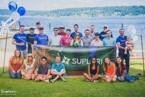 A Group Of People Standing In Front Of A Beach Holding A Green Suplari Banner