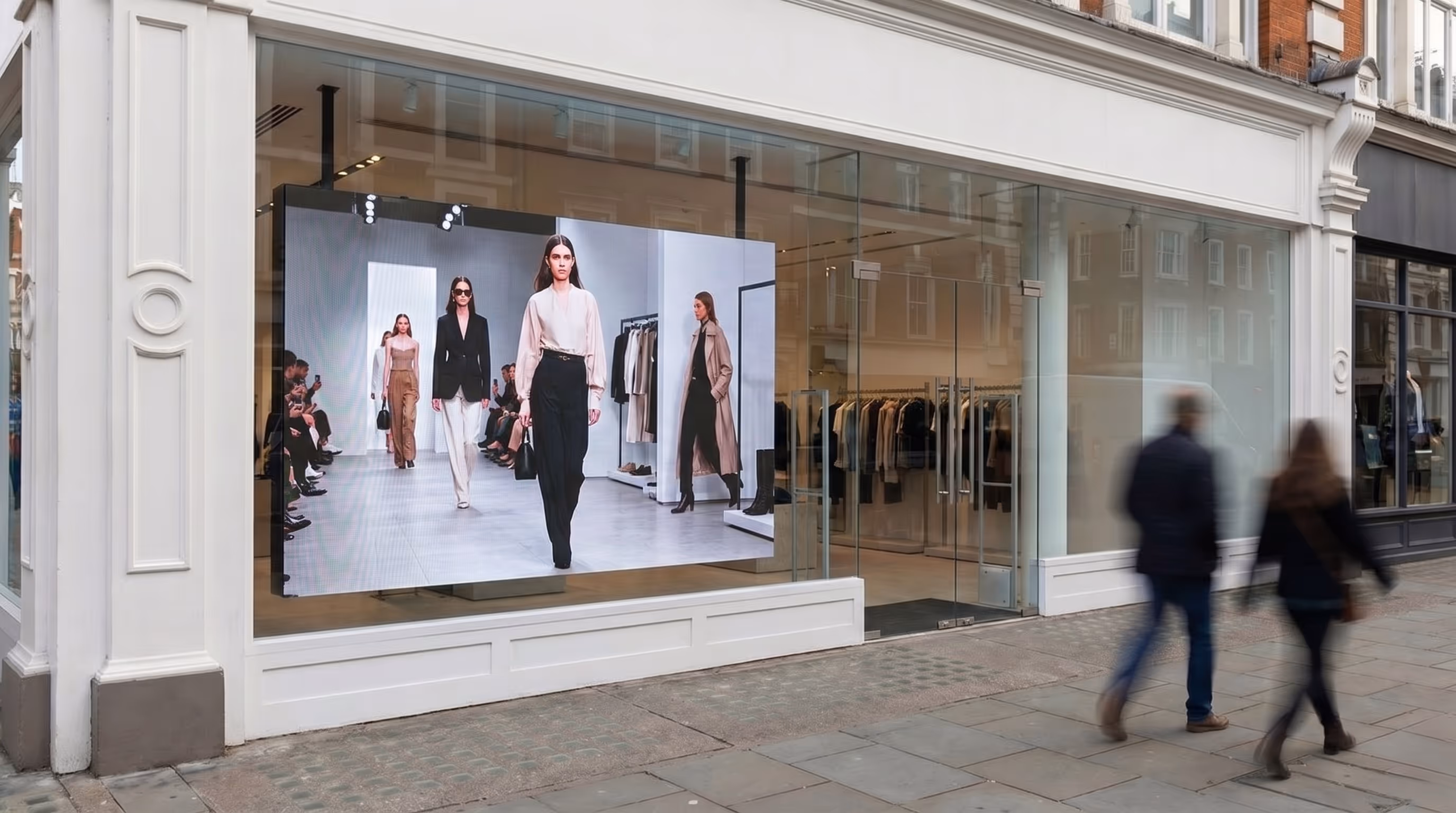 Fashion store window with a large digital display showing a runway with models walking.