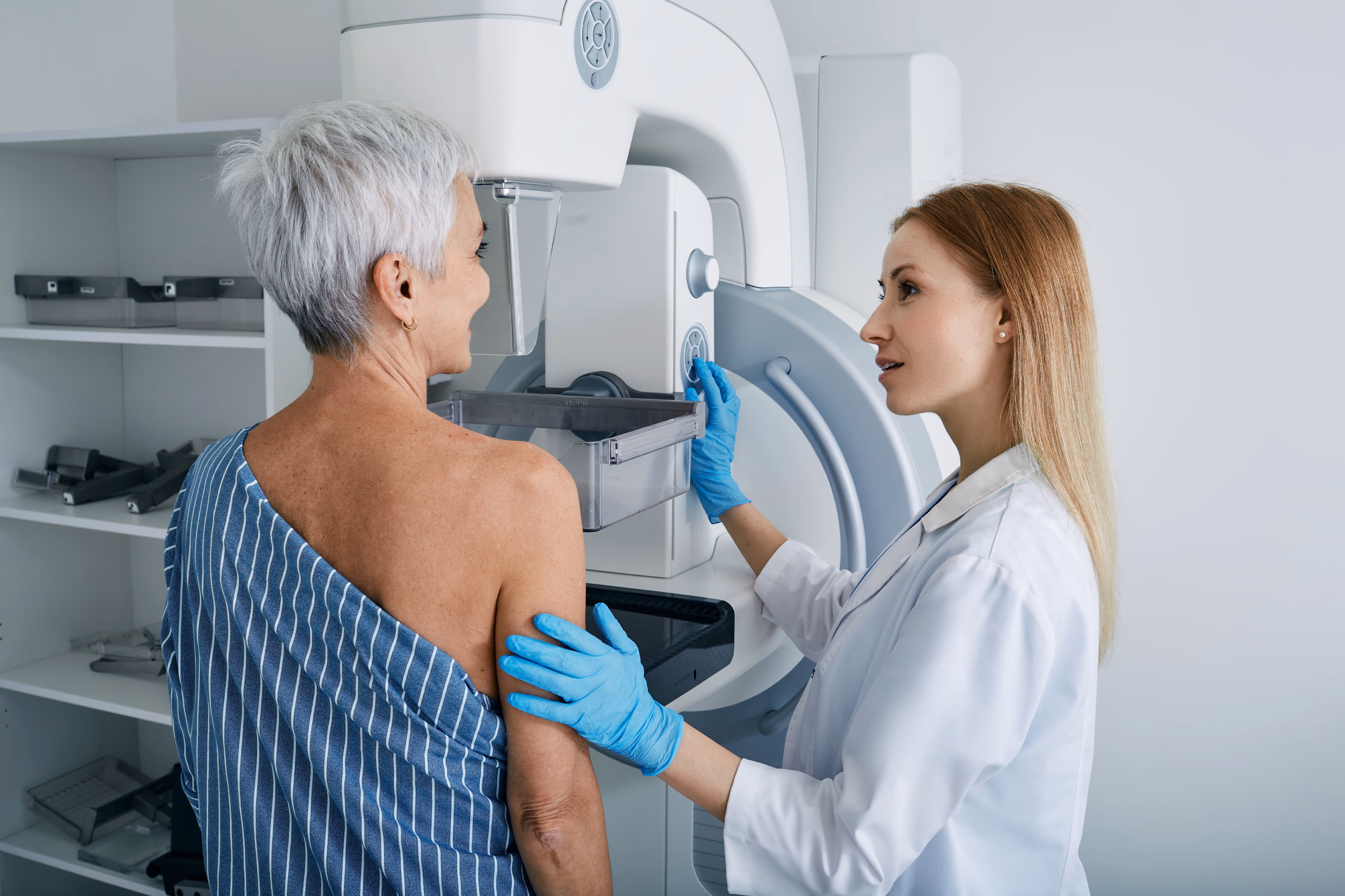 A woman with short hair is having a mammogram taken while a female doctor in a lab coat comforts her.