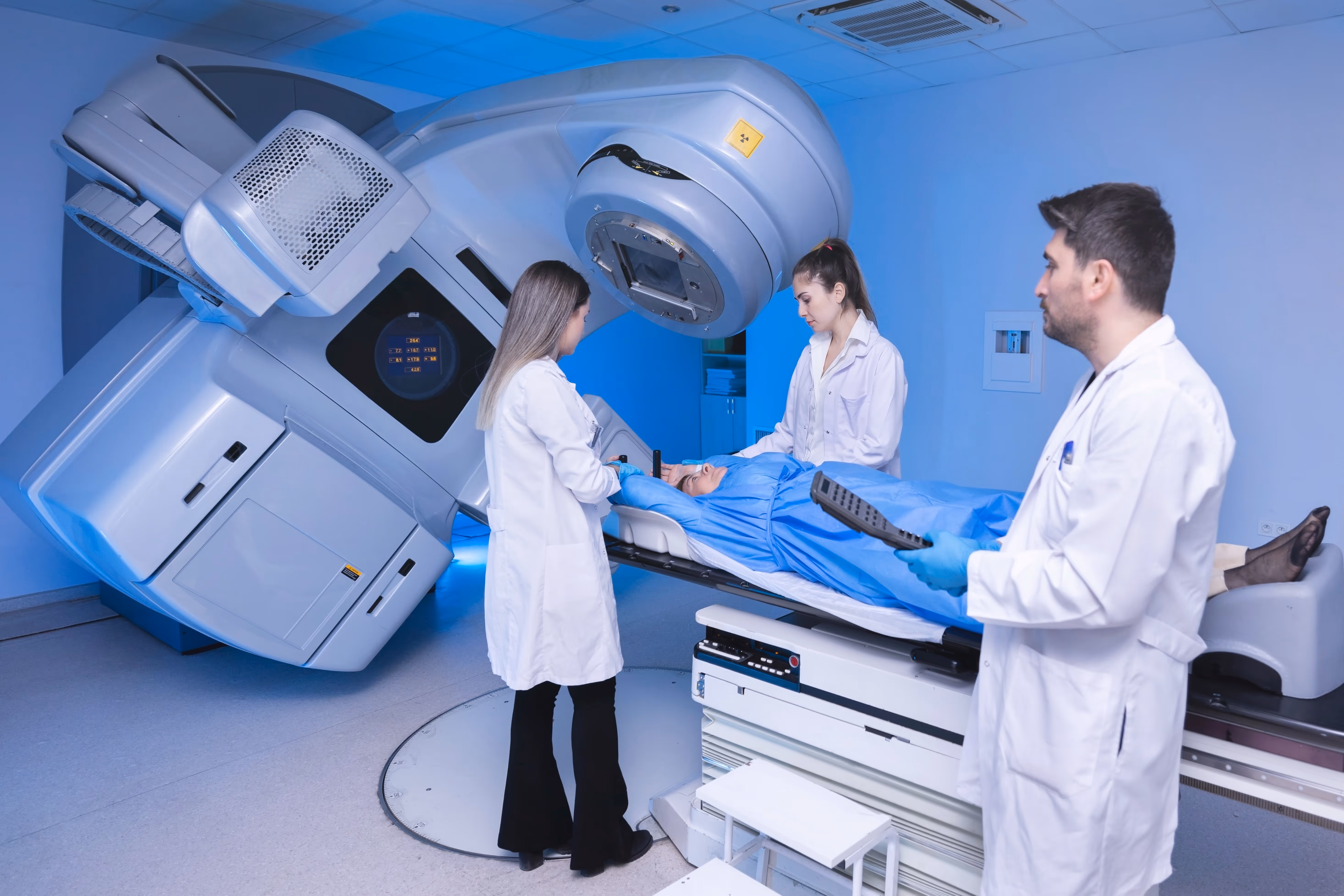 Three medical providers in lab coats surround a patient lying flat as they have an X-ray taken.