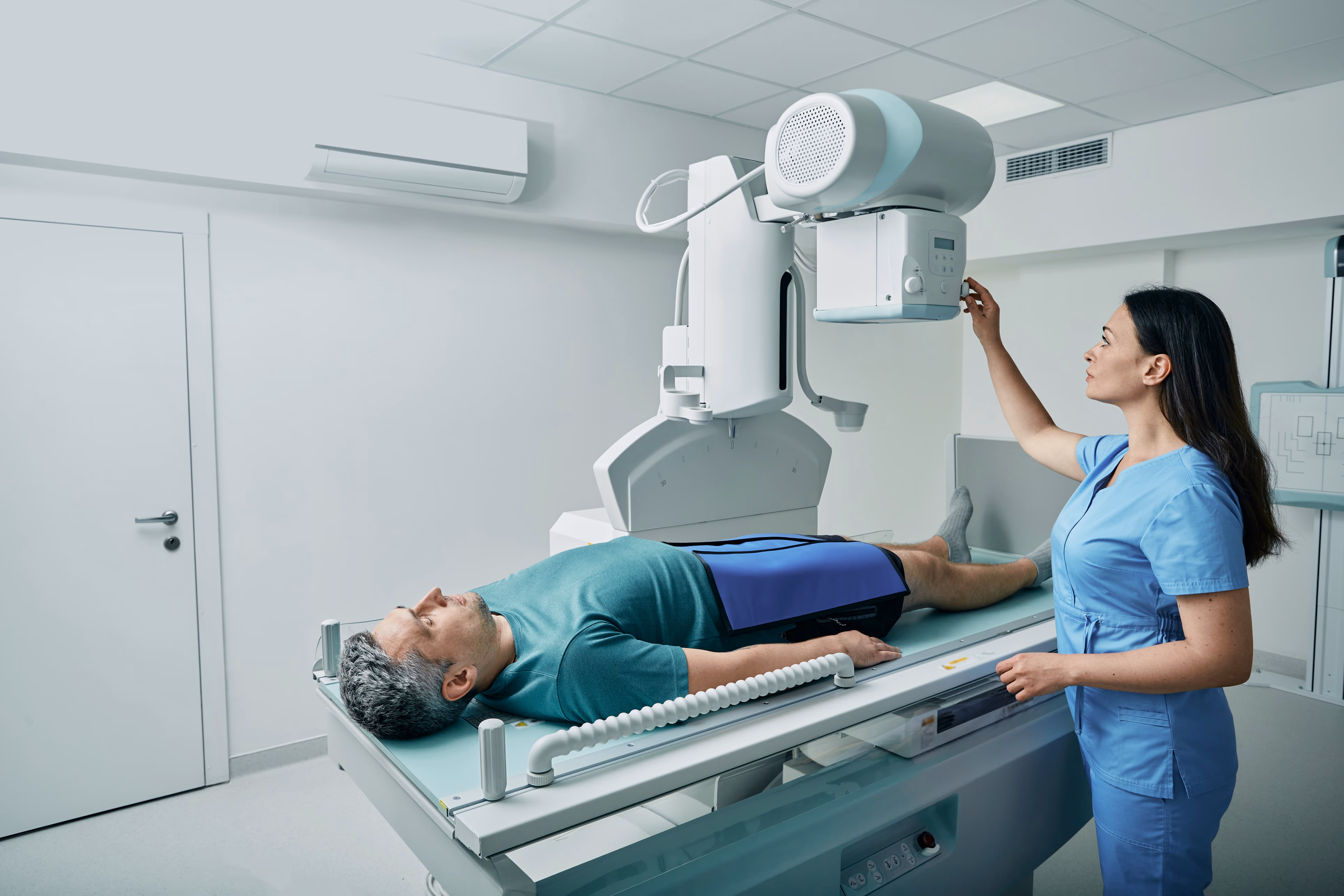 A man is lying down as a woman in scrubs works on an x-ray machine to getting imaging done.