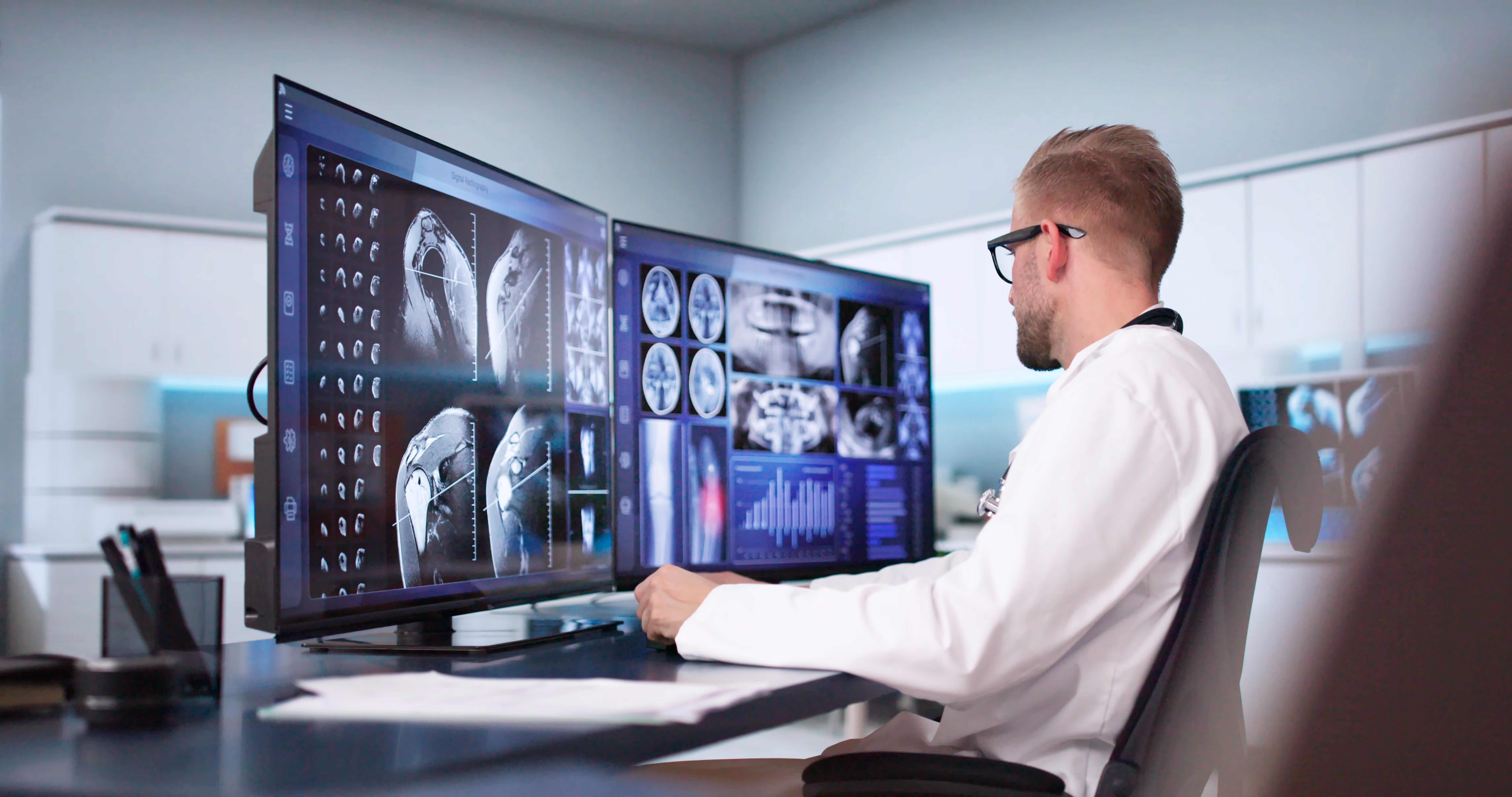 A radiologist looking at two computer monitors with medical images pulled up.