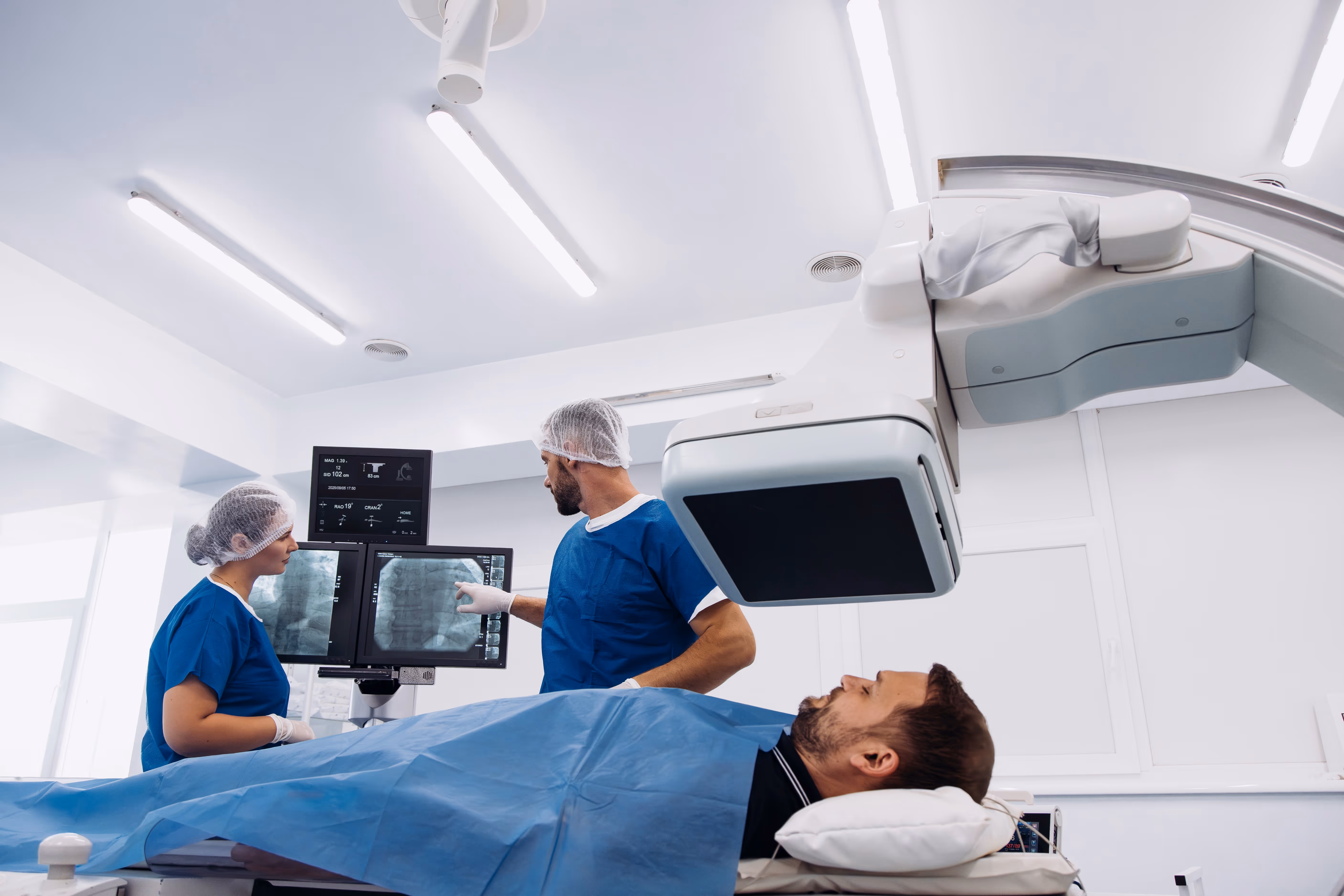A man lays on a surgical bed as two medical professionals review an image and prepare for a procedure.