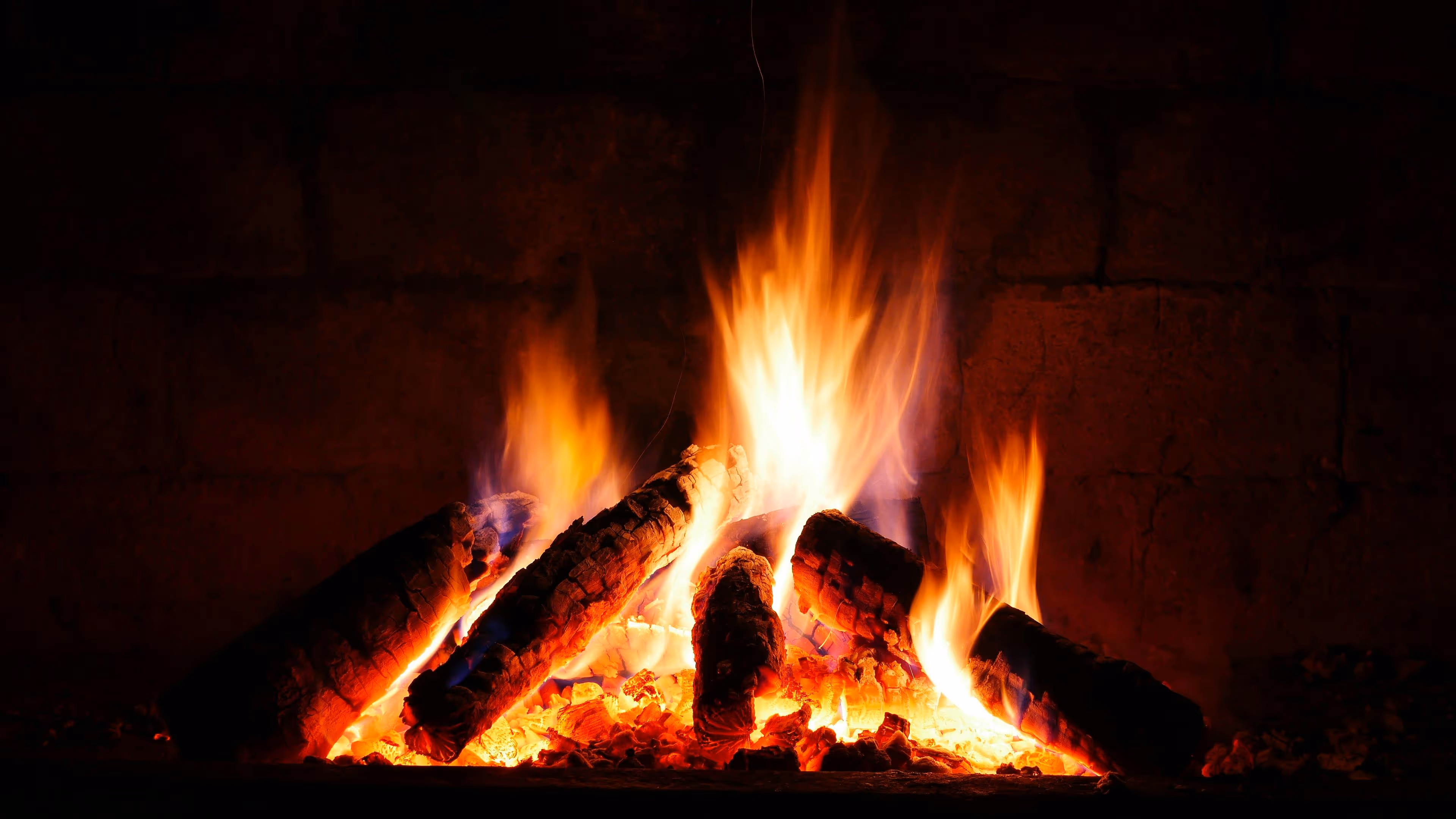 Bright orange and yellow flames burning large logs on glowing embers in a fireplace.