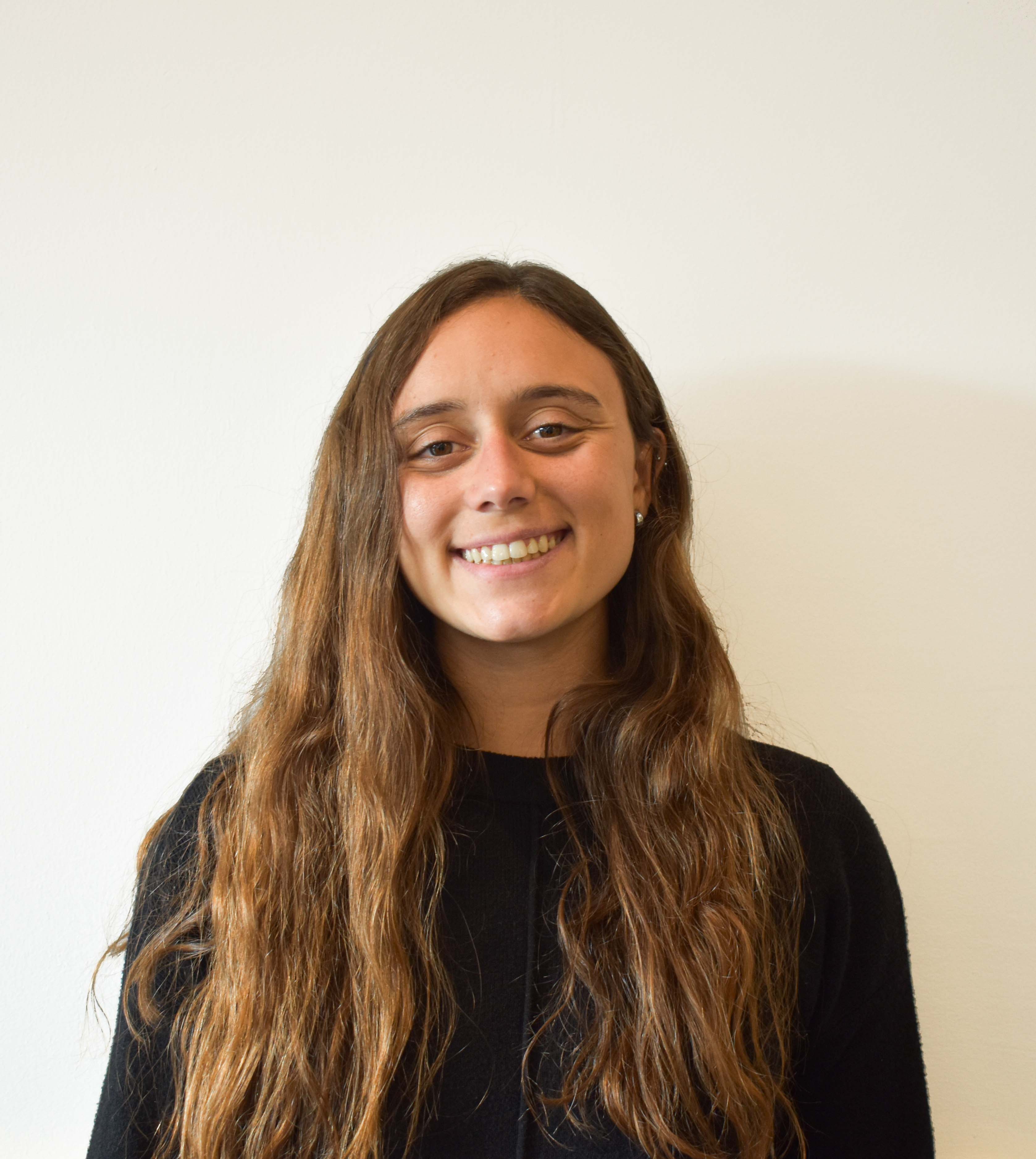 Mujer sonriente con cabello castaño largo y suelto, vistiendo un suéter negro.