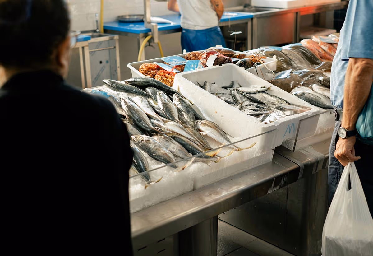 Fresh fish and seafood displayed on ice at a market with customers nearby.