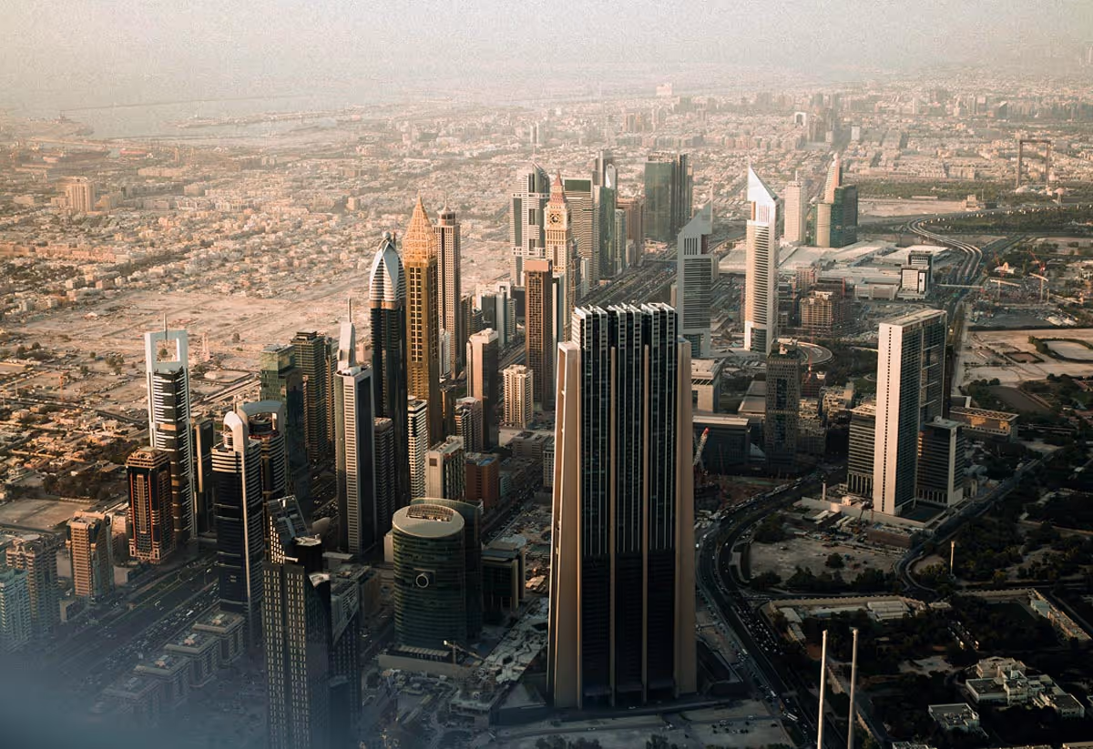 Aerial view of a Dubai cityscape featuring tall modern skyscrapers and sprawling buildings under hazy sky.