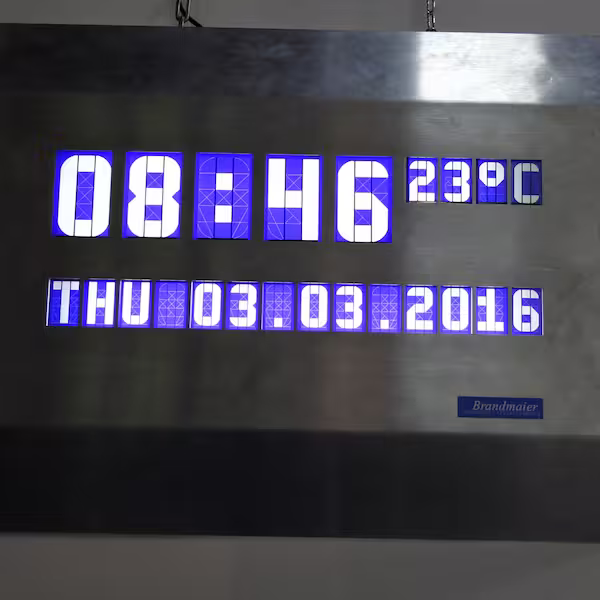 Large display board on a stainless steel plate with blue and white digits for time, temperature and date