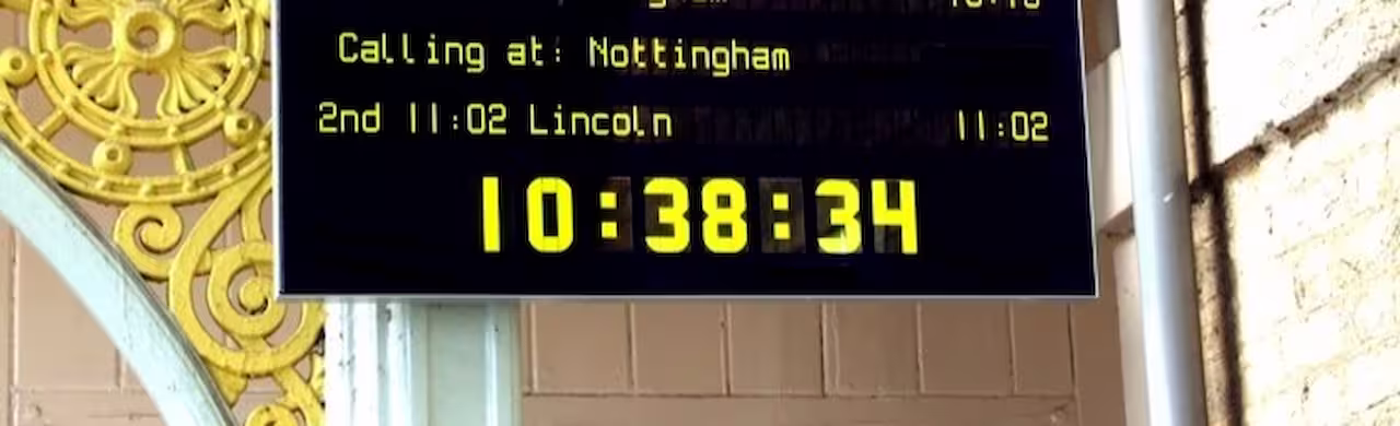 Yellow glowing train display with route and running time under an ornate station hall