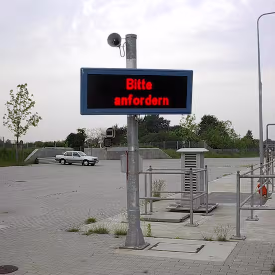 LED display on a pole above an empty yard area, red text Bitte anfordern