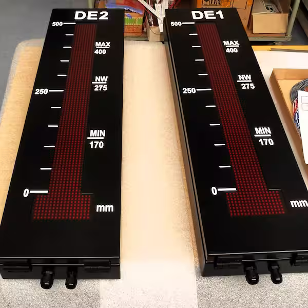 Two portrait-format LED bar graph displays with a millimetre scale and MIN/MAX marks in a workshop