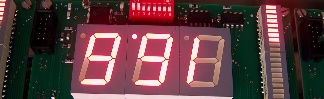 Close-up of a circuit board with large red seven-segment digits and DIP switches