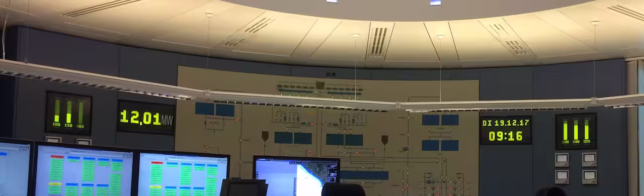 Leitwarte mit Monitoren, Wandschema und LED-Anzeigen für Leistung, Datum und Uhrzeit