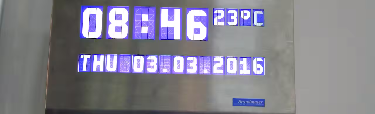 In eine Metallplatte eingelassene Anzeige mit Uhrzeit 08:46, 23 °C sowie Wochentag und Datum