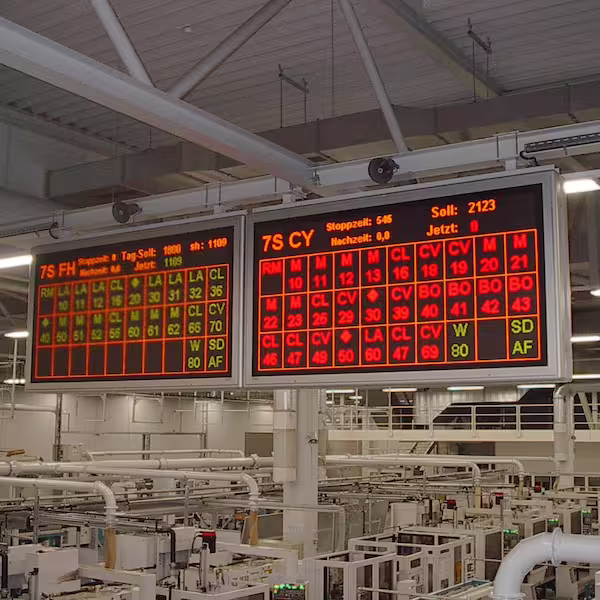 Two large LED boards with production data hanging below the hall roof above the shop floor