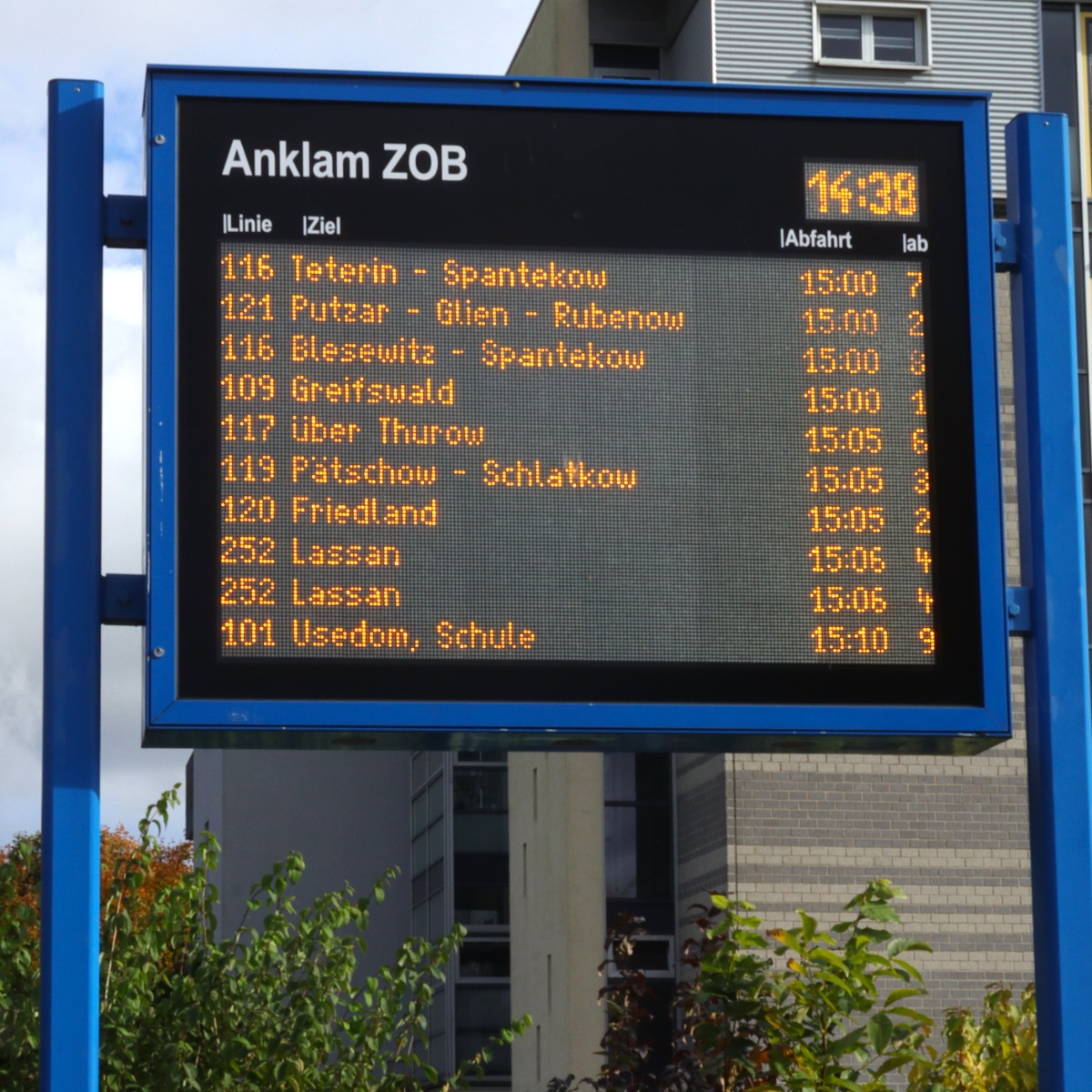 Display board in a blue frame with orange text showing bus lines, destinations and times at a bus station