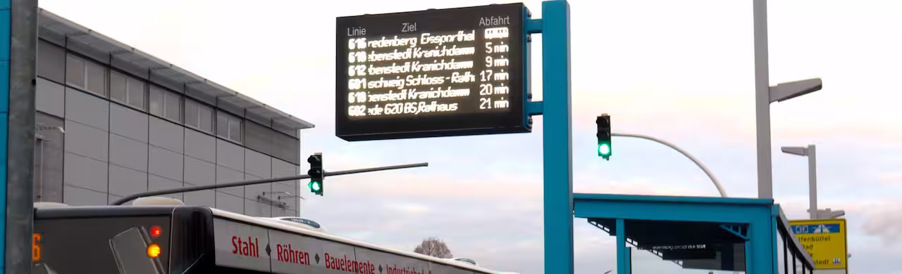Fahrgastanzeige an einem Ausleger über dem Busbahnhof, darunter Busse und Ampeln