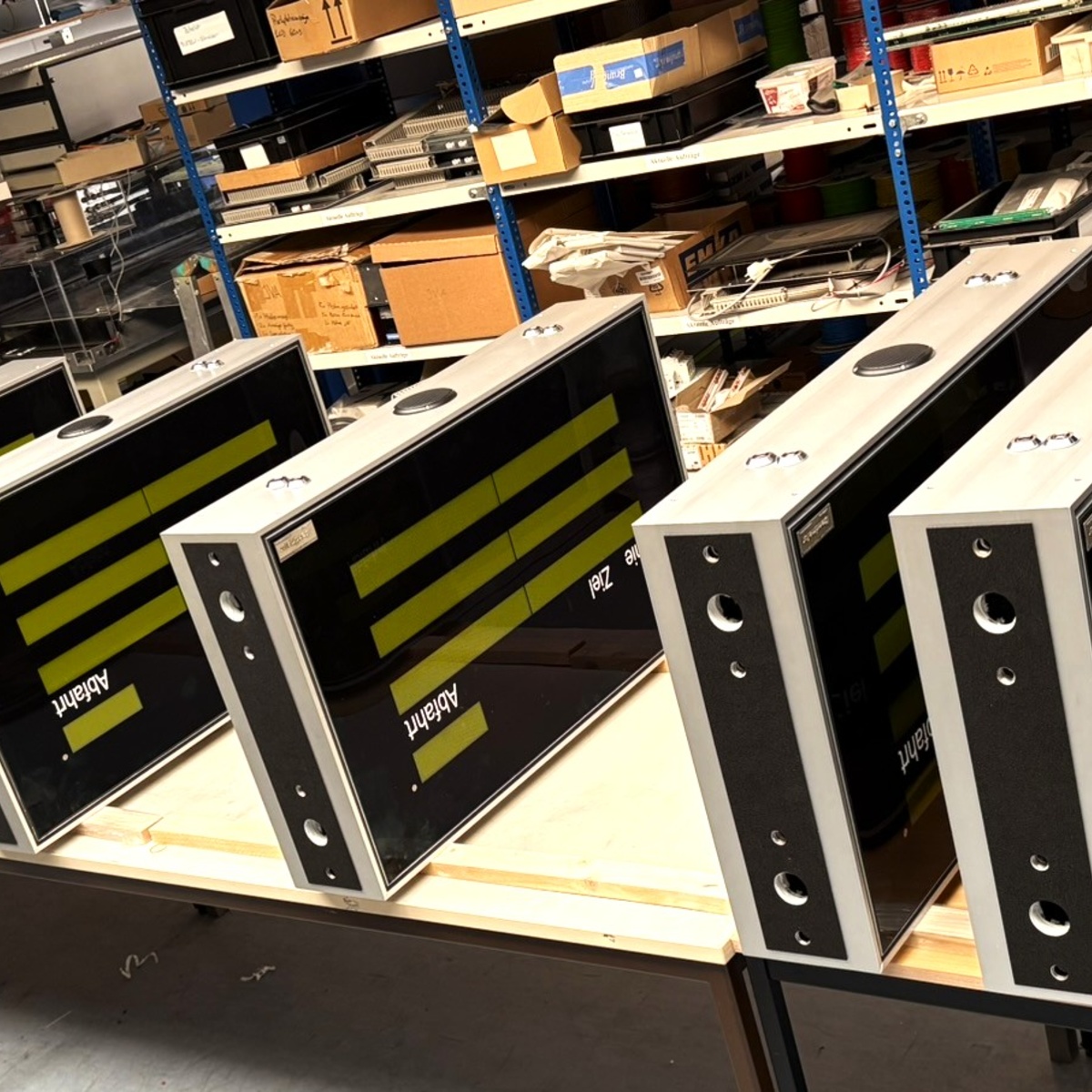 Several flat display housings lined up on a pallet in a warehouse with shelving