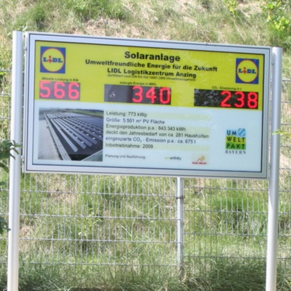 Freistehende Infotafel zu einer Solaranlage mit drei großen roten LED-Zahlenfeldern vor einer Grünfläche