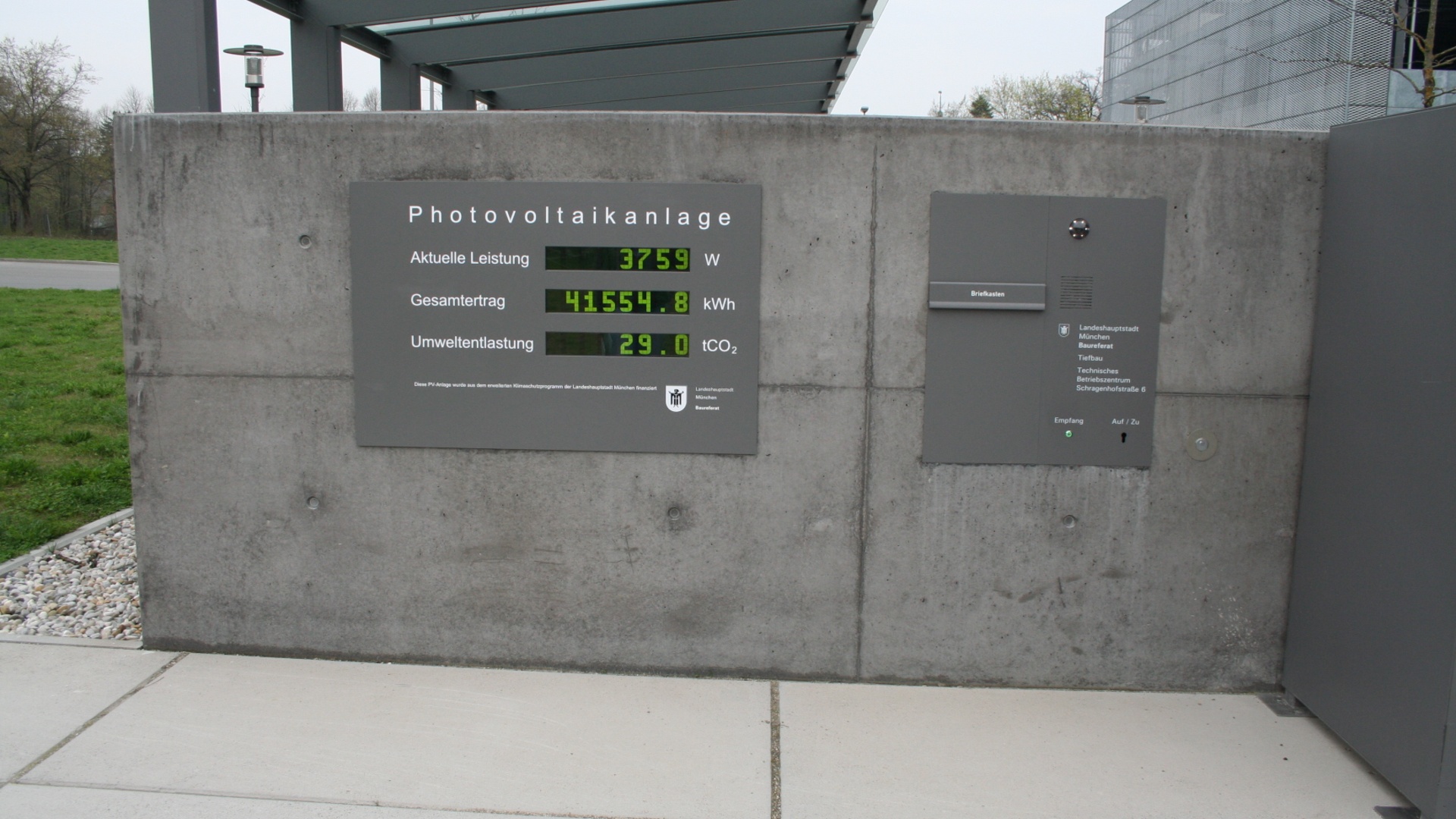 Anzeigetafel einer Photovoltaikanlage mit grünen Ziffern zu Leistung, Ertrag und CO2 an einer Betonwand