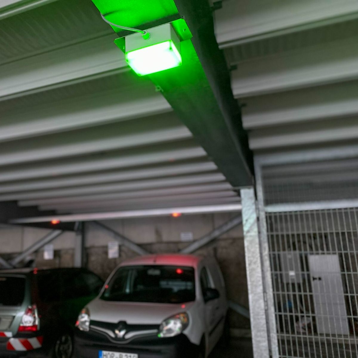 Grün leuchtender Stellplatzmelder an einem Deckenträger über einem weißen Transporter im Parkhaus