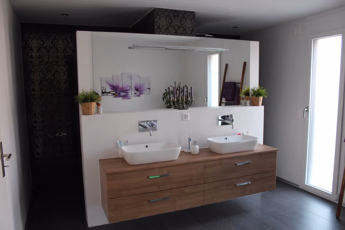 Modernes Badezimmer mit großem Spiegel, zwei weissen Waschbecken auf einem schwebenden Waschtisch aus Holz, Pflanzen in Weidenkörben und einer Milchglastür.