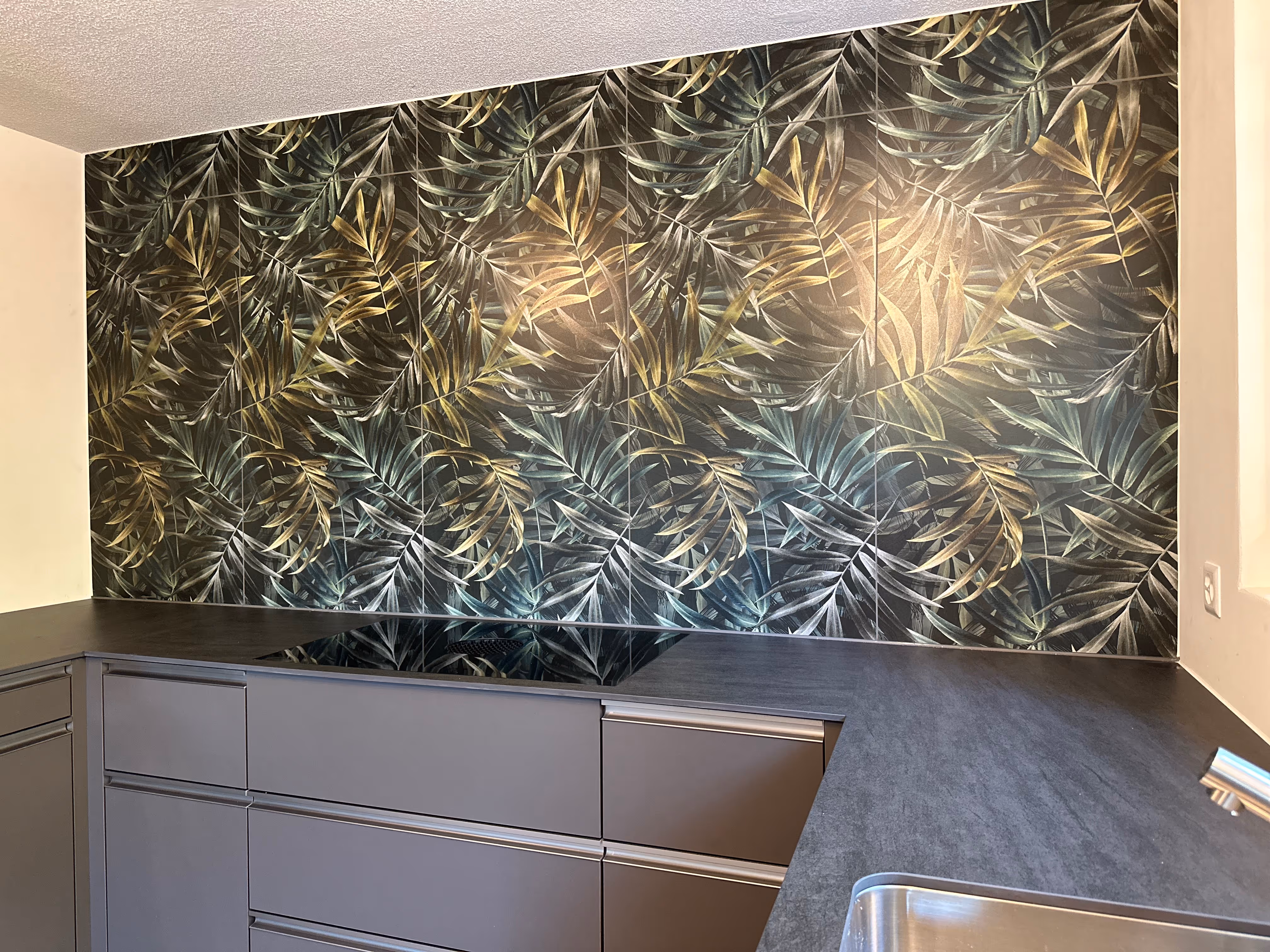 Moderne Küchenrückwand mit dunklen Fliesen mit Blattmuster über grauen Schränken und einer schwarzen Arbeitsplatte mit Spüle.