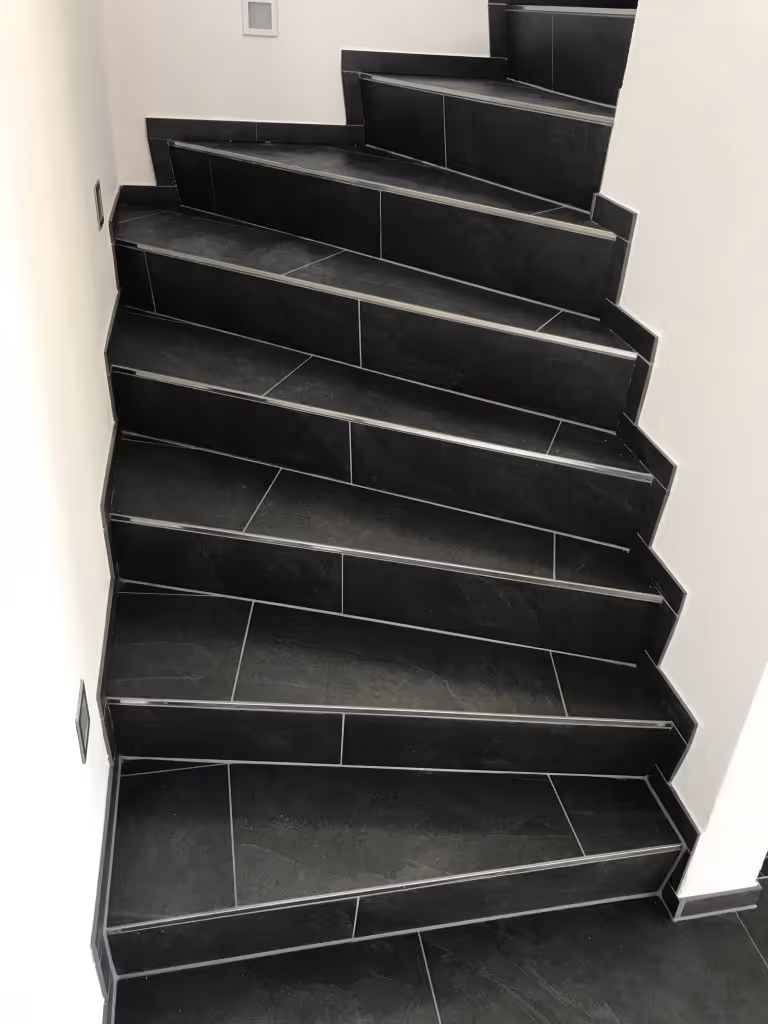 Innentreppe mit schwarzen rechteckigen Fliesen und weissen Wänden auf beiden Seiten.
