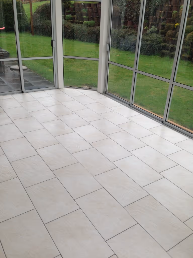 Wintergarten Raum mit grossen Glasfenstern und weissem Fliesenboden mit Blick auf einen grünen Garten.