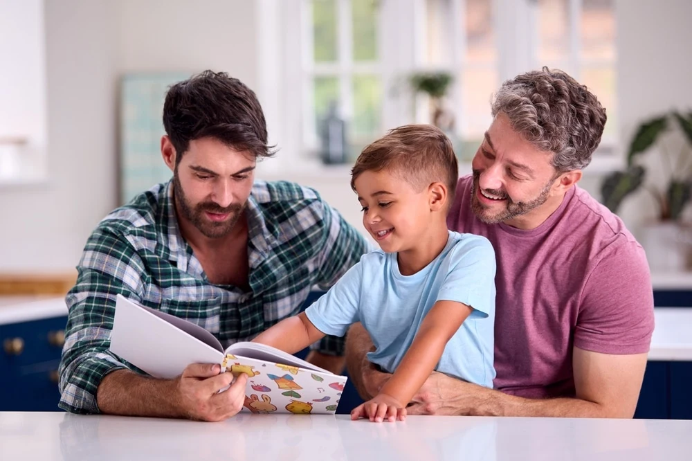 8:43 PMClaude responded: Two dads reading a picture book with their young son at the kitchen counterTwo dads reading a picture book with their young son at the kitchen counter