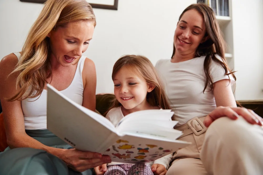 Nanny reading a picture book with a young girl while mother looks on at home