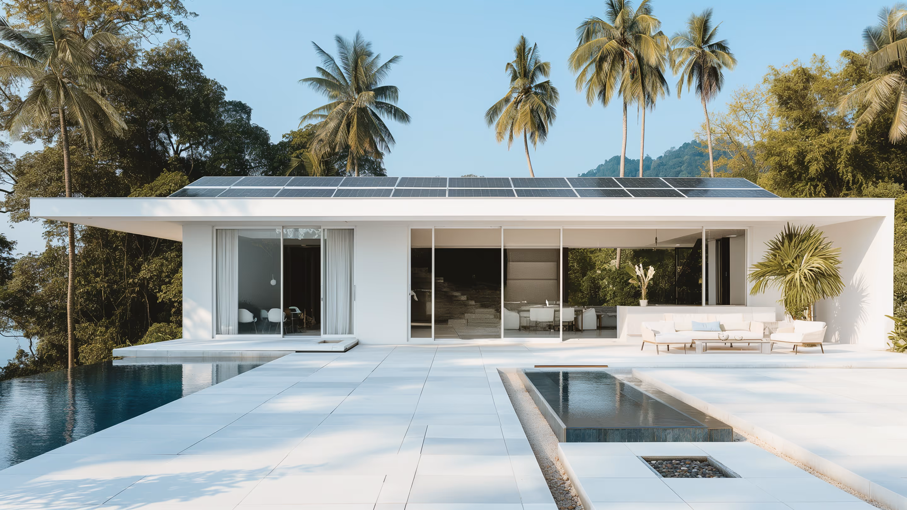 Современный белый дом с плоской крышей и солнечными панелями, окружённый пальмами, с бассейном на открытом воздухе.