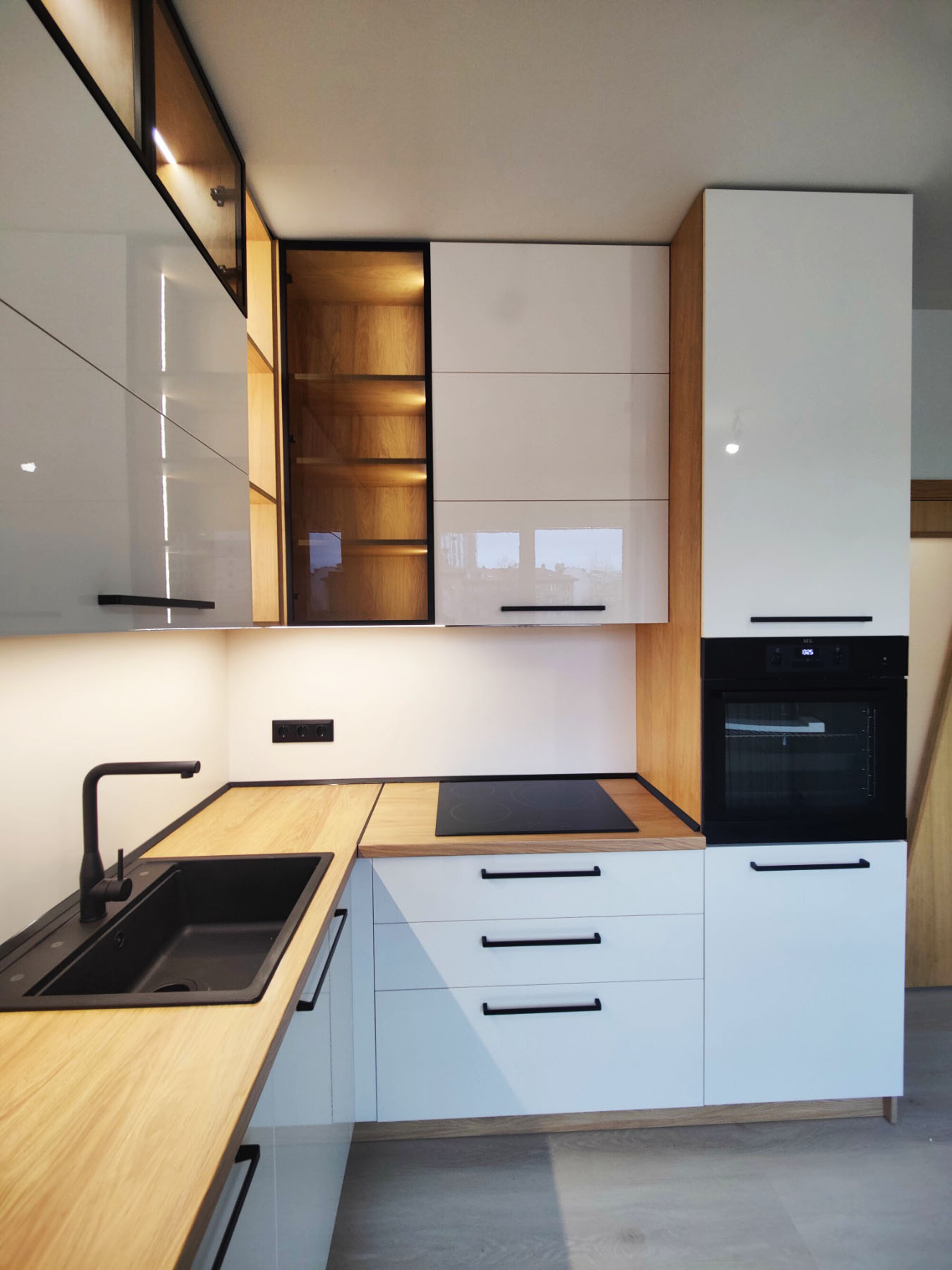 Детайл работен ъгъл с черна мивка и котлони, осветени ниши и висока колона; EGGER H3730 ST10 корпус/плот, Kronospan 0564 HG/BS лице, 0564 PE гръб.