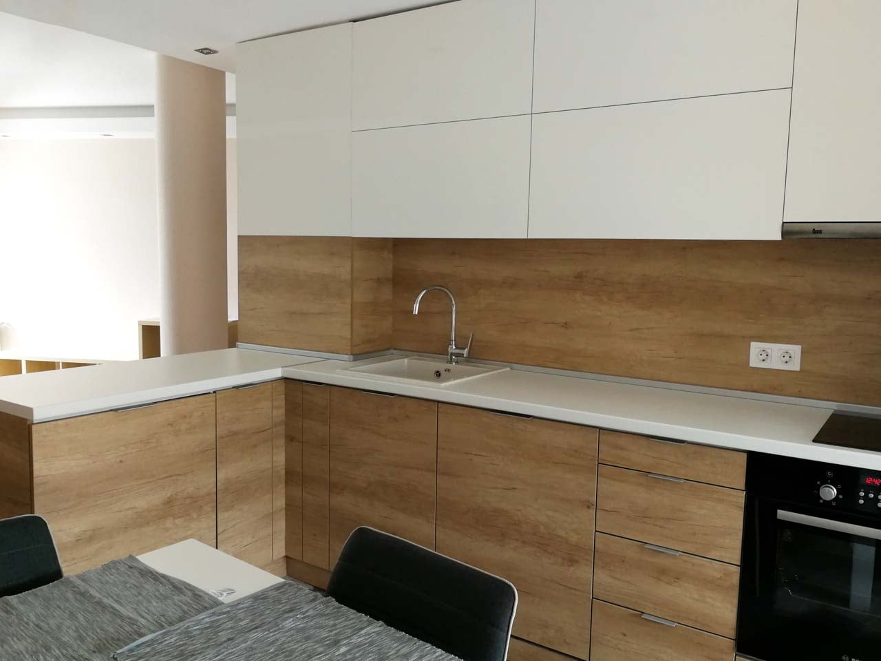 Детайл на работната зона с мивка FAT, бели гланцови горни шкафове, дъбов гръб и долни шкафове в дъб, светъл плот и вградена фурна.