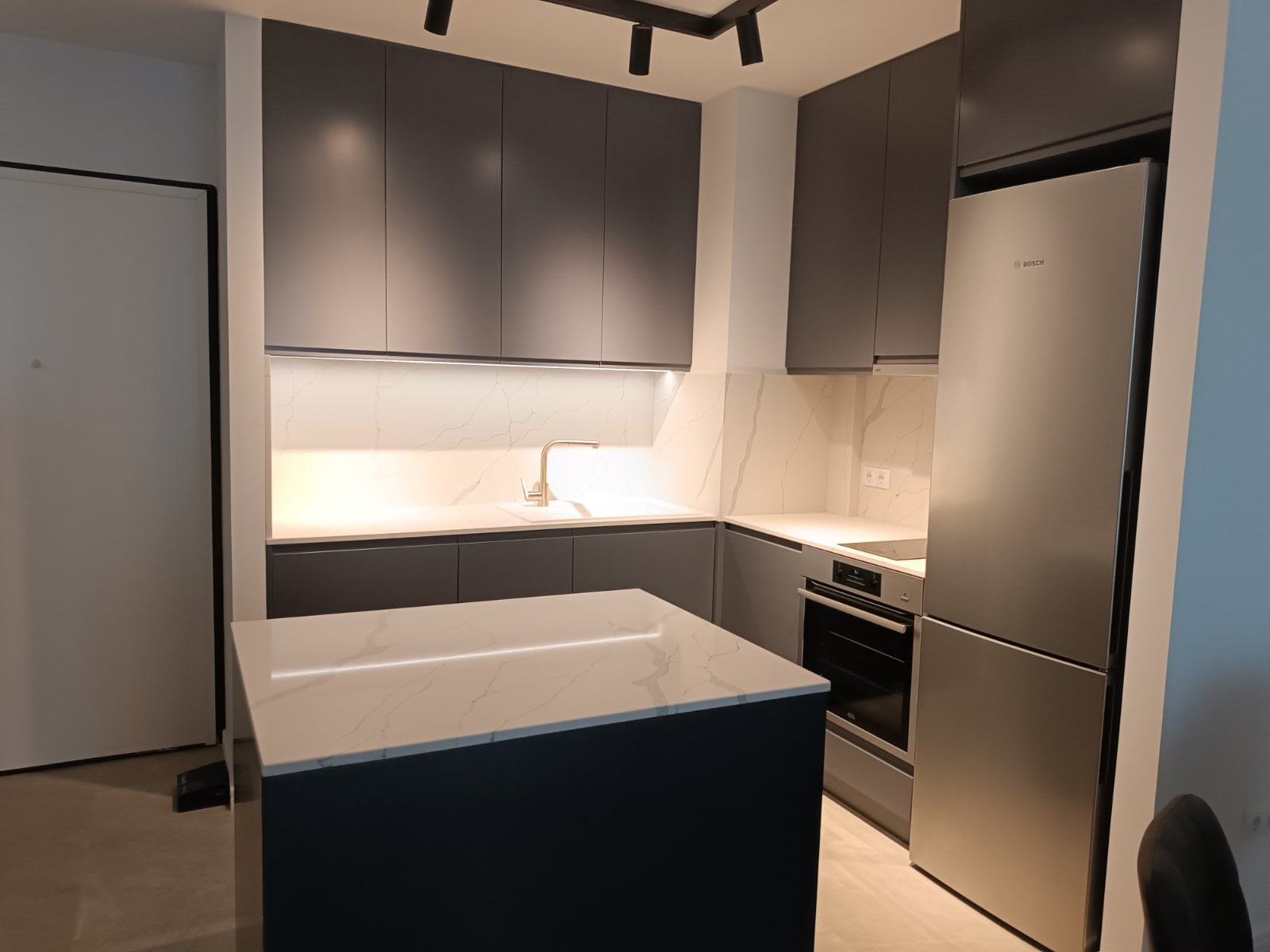 Ъглова кухня с остров в мат RAL 7043 и фрезовани дръжки, плот и гръб от технически камък Crystal Calacatta Amnis TECHNISTONE, механизми Blum. Модерна кухня по поръчка с остров и вградена техника.