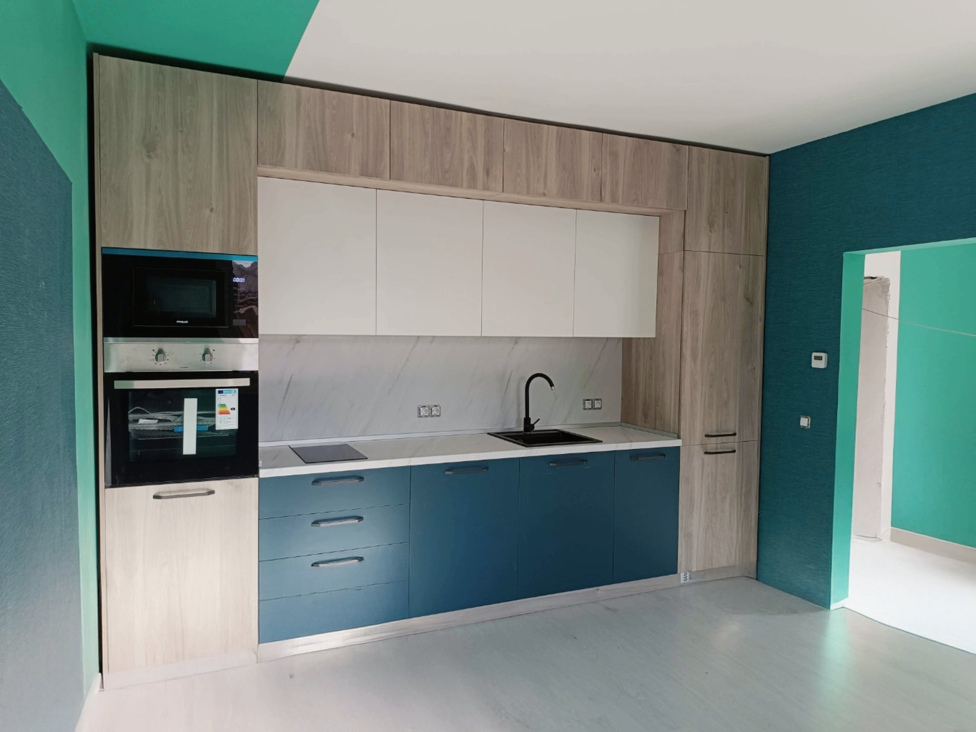 Ъглова модерна кухня по поръчка със светли гланцови шкафове, плот светъл дъб, черни дръжки и LED осветление.