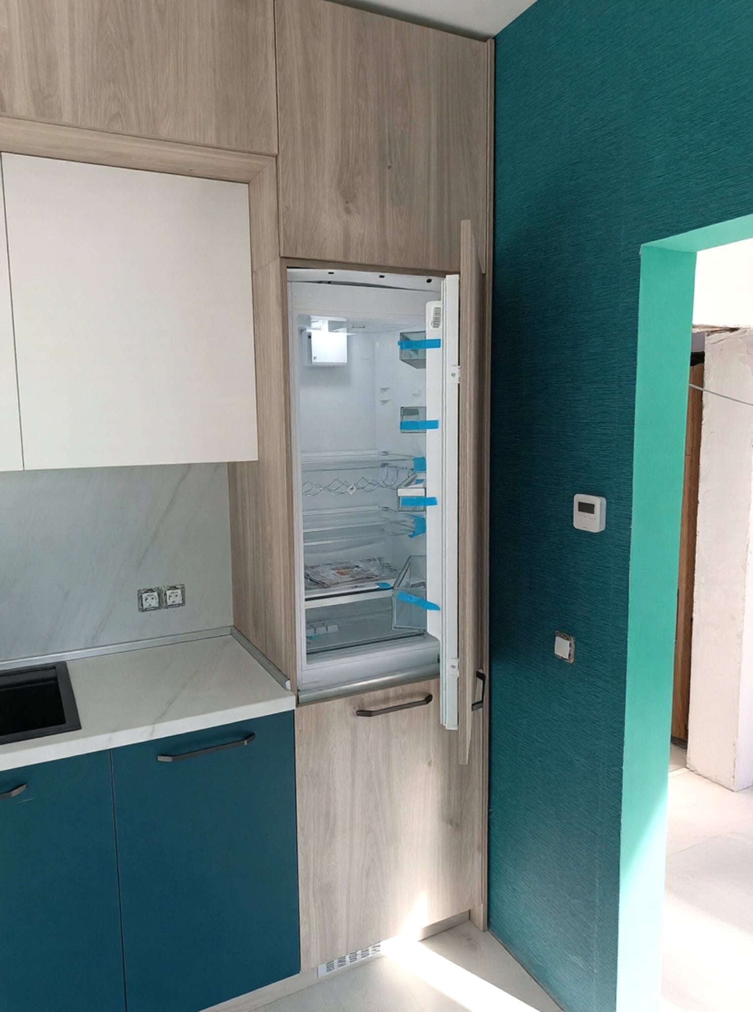 Детайл на колона с вграден хладилник и високи шкафове; равни фронтове и дискретни дръжки, прецизно напасване към стената.