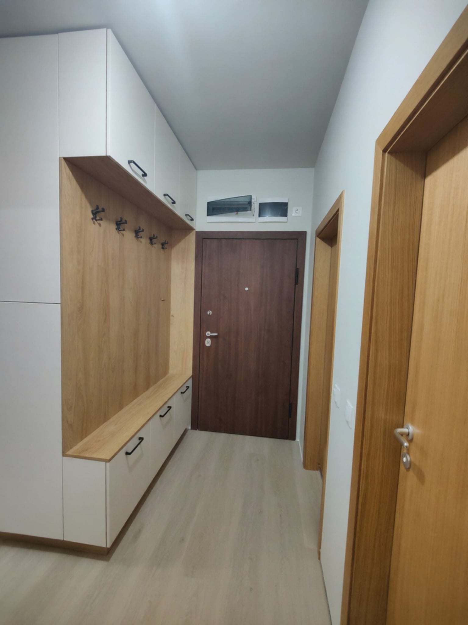 Коридор с високи шкафове до таван и плавни линии, комбиниращ каме мат фронтове и естествен дървесен корпус.