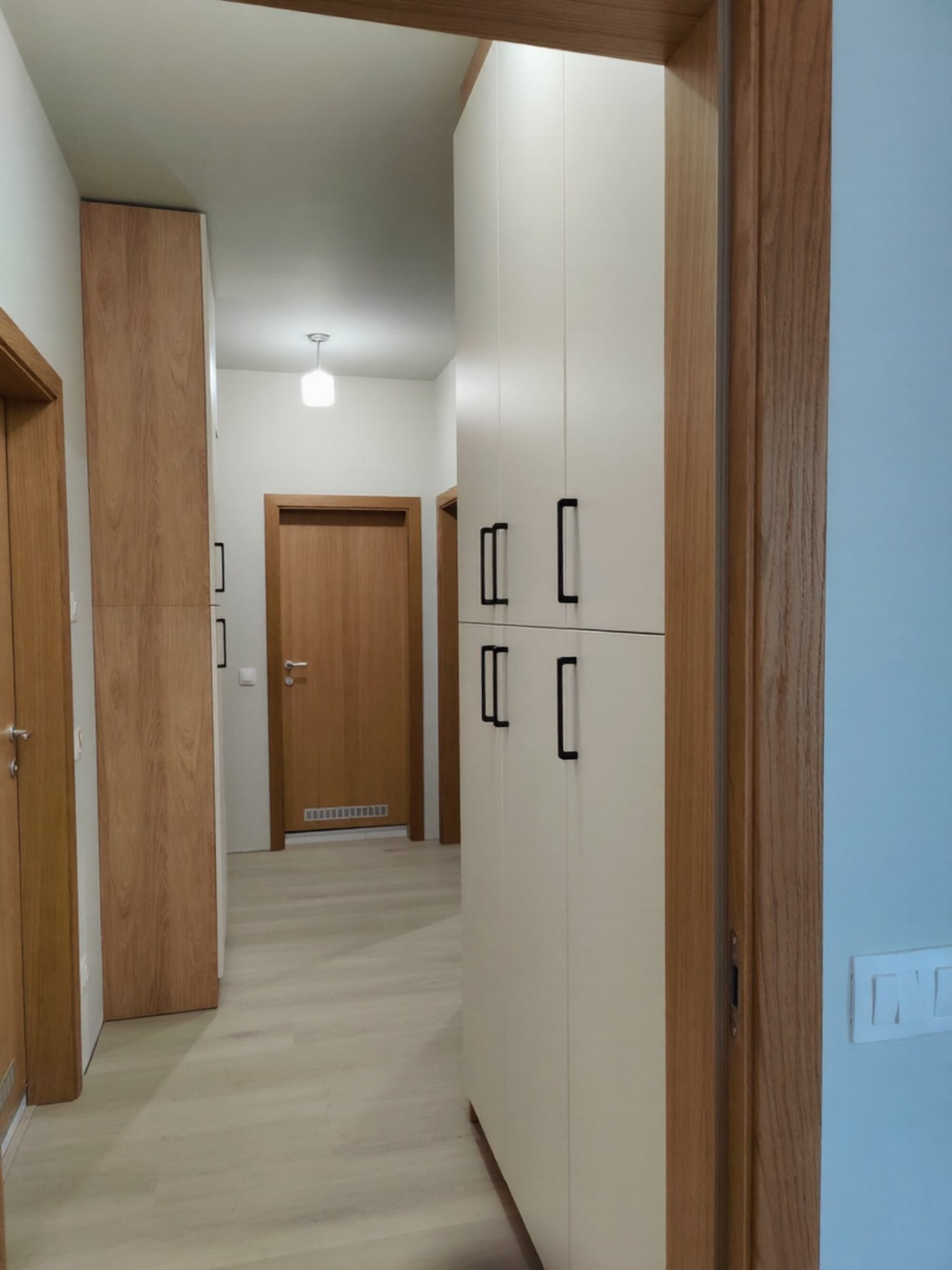 Входна зона с открита ниша за закачалки и пейка, облицована с хикори натур и черни метални закачалки