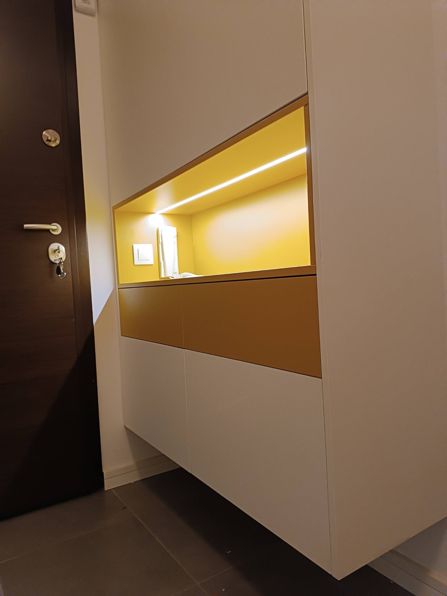Коридор по поръчка с вградени шкафове и осветена ниша. Светли повърхности с топъл цветен акцент за модерен и функционален вход.