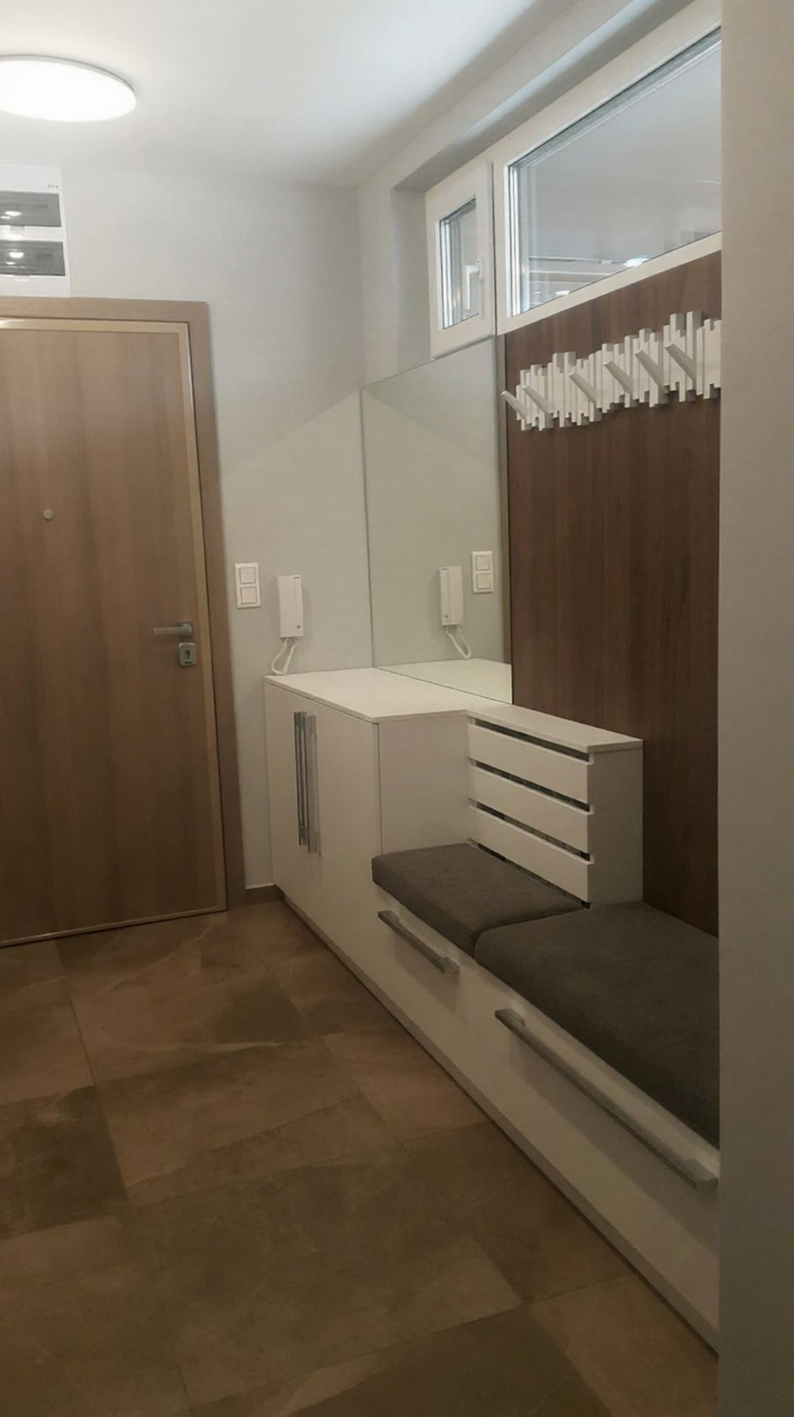 Коридор по поръчка с вградени шкафове, бели лица и дървесен акцент. Практично разпределение, включващо интегрирани купички за домашен любимец.