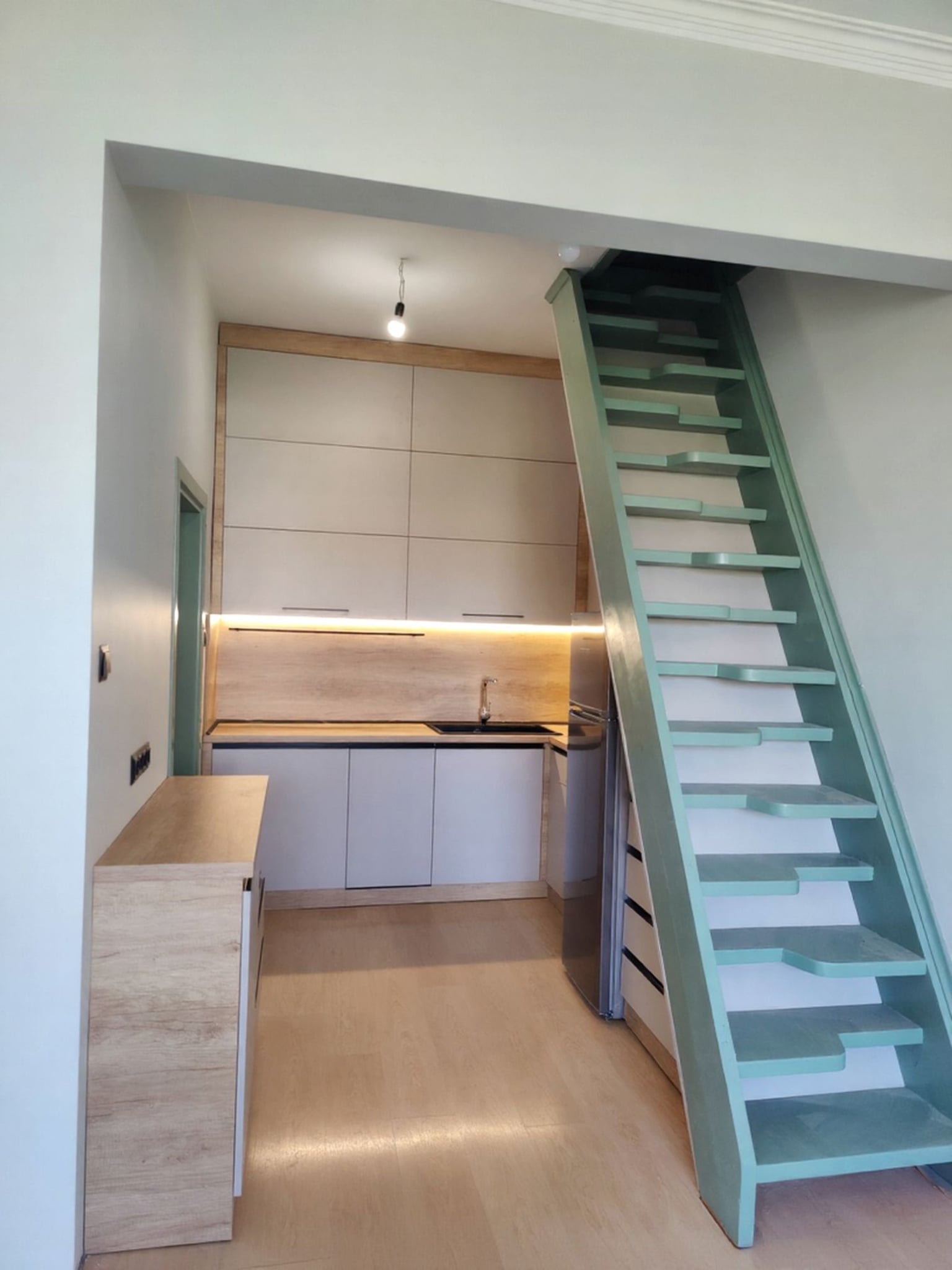 Кухня по поръчка за малко пространство с максимална функционалност – кашмирени лица, декор дъб Небраска за топлина и визуална дълбочина, L-образен работен плот и решения около стълба. Проектирана за реалния живот, а не по стандарт.