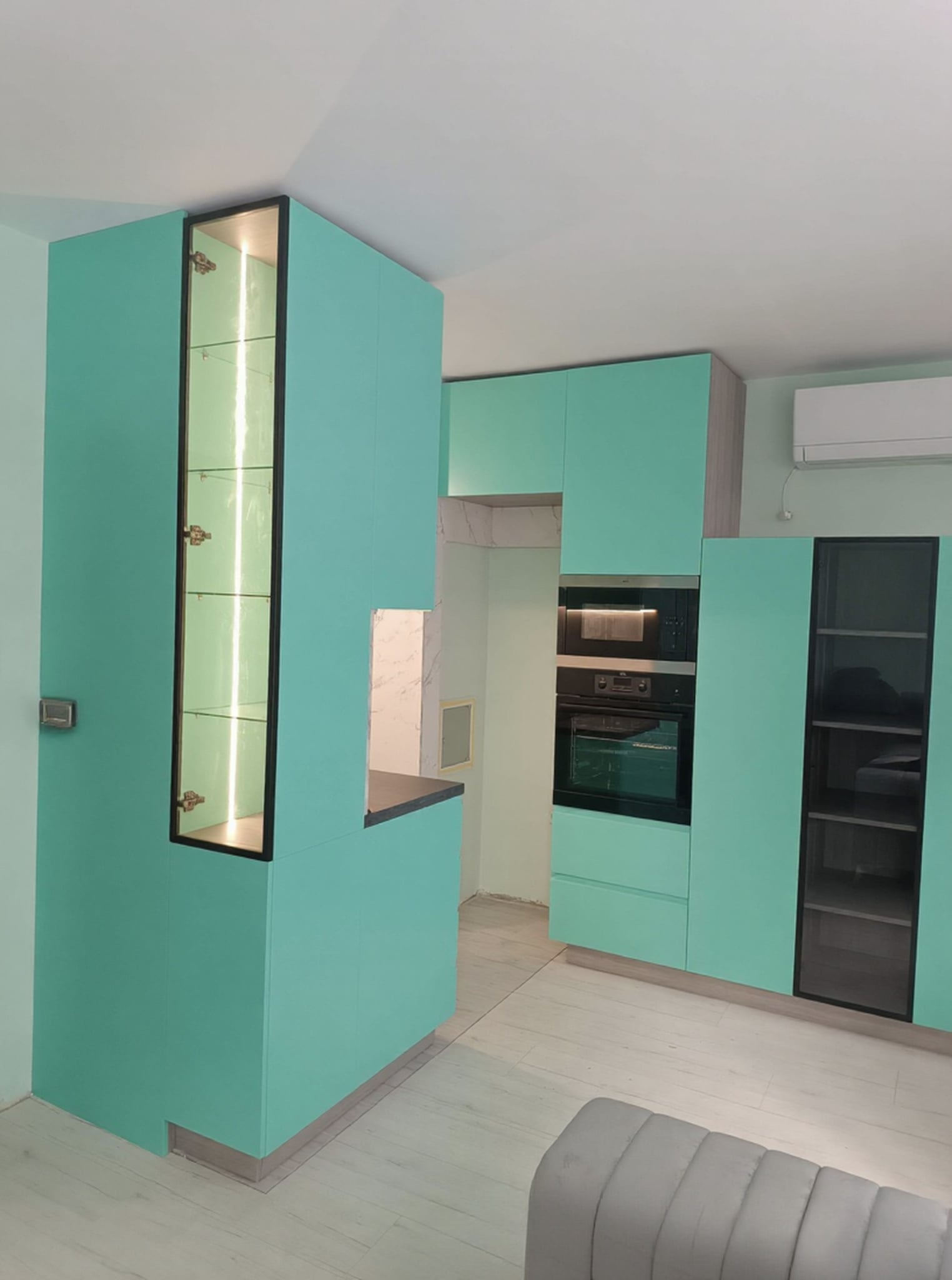 Висок шкаф с вградени фурна и микровълнова и витрина с черна рамка и вътрешно осветление.