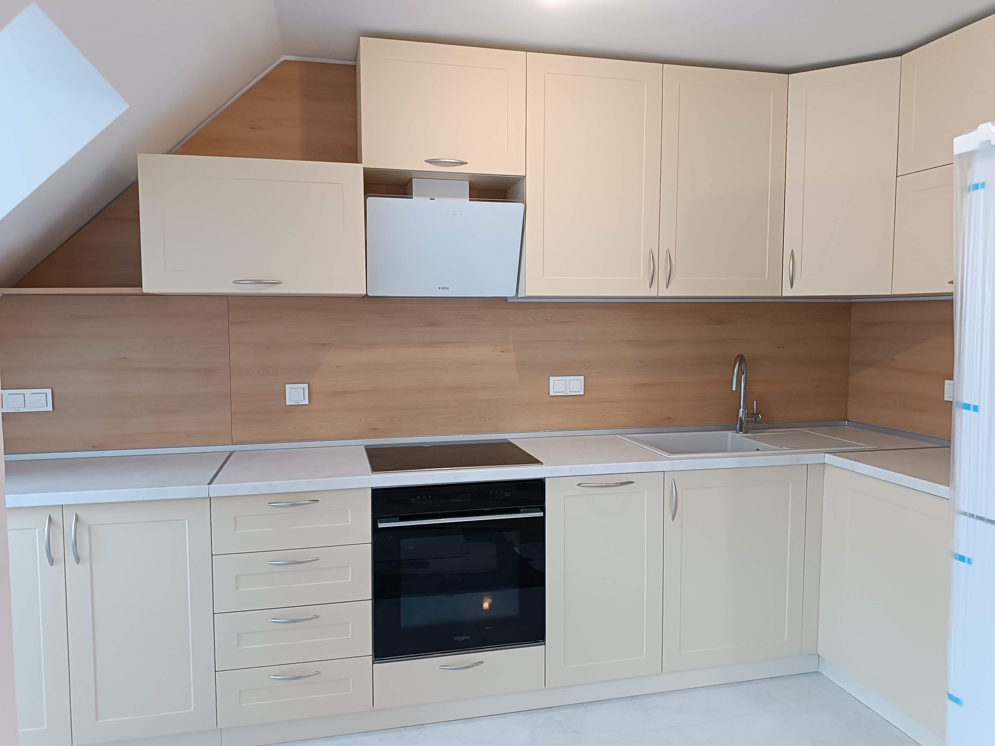 Общ изглед към кухнята в подпокривно пространство със скосен таван и завършена линия от горни шкафове.