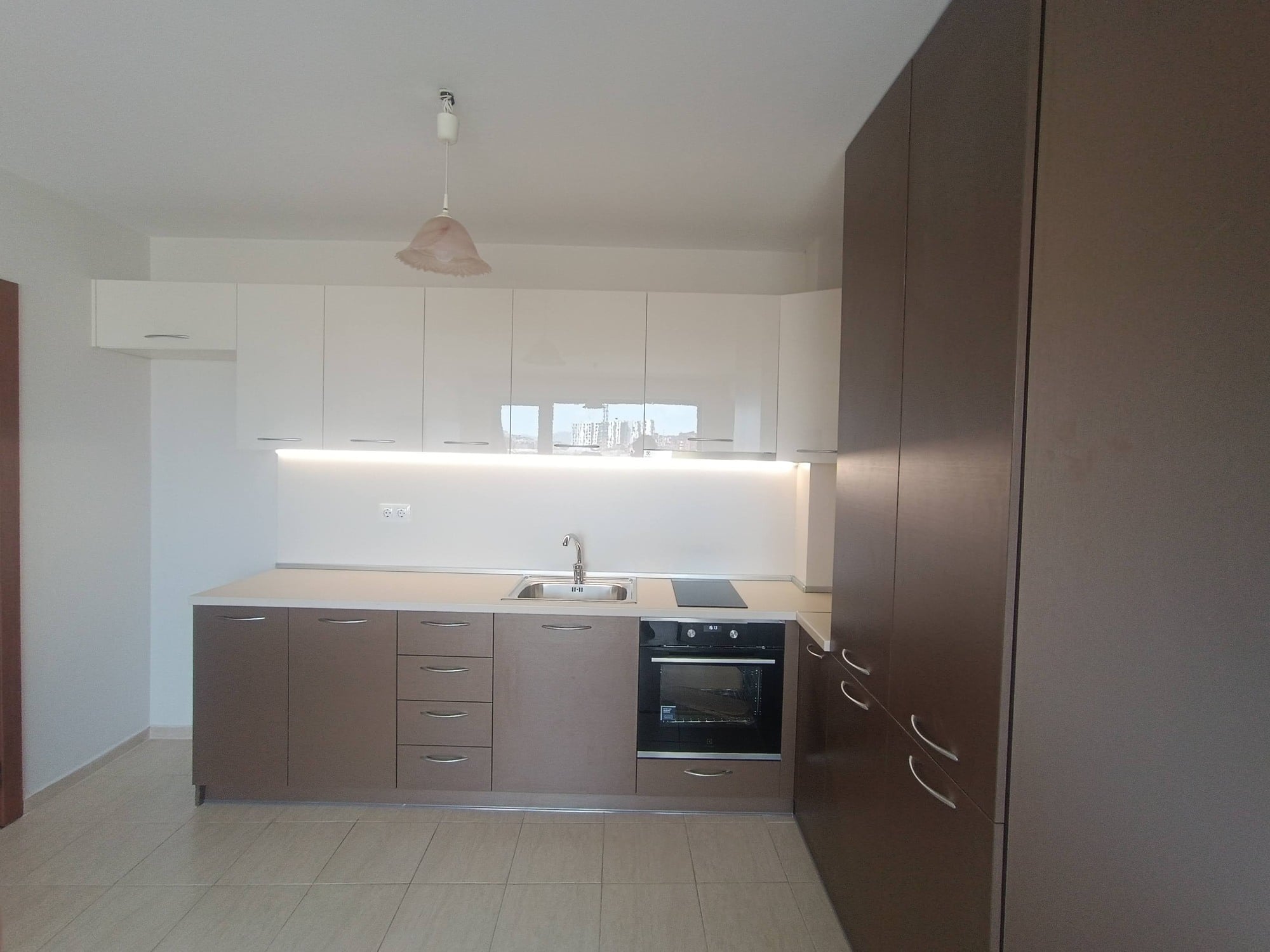 Общ изглед към работната зона с вградена фурна и плавен преход към високия бронзов шкаф.