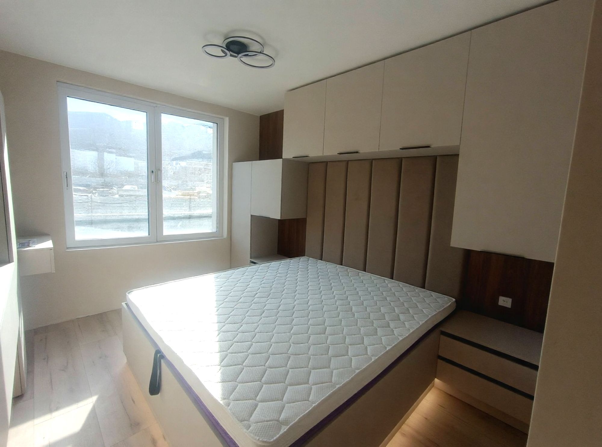 Спалня по поръчка в кашмир PerfectSense мат и тъмен дъб Чарлстон EGGER с тапицирана табла, висящи нощни шкафчета с LED и ТВ зона с тоалетка. Модерно решение с хотелско излъчване и максимален комфорт.