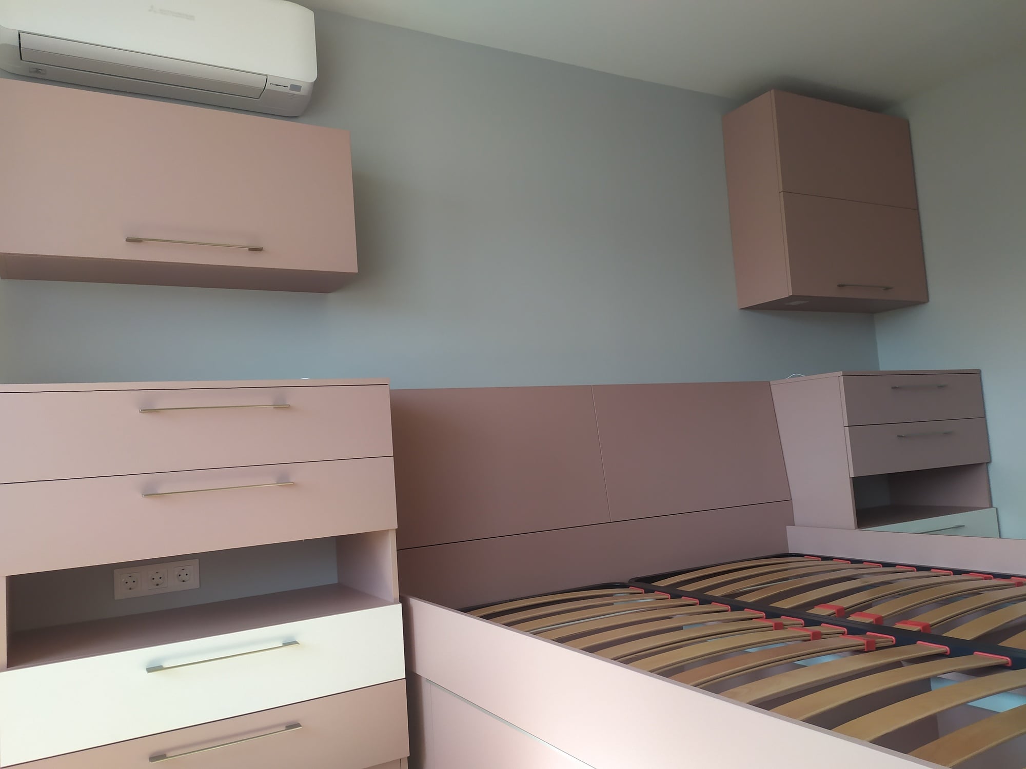 Композиция от шкафове около леглото с работна зона и вградени контакти.