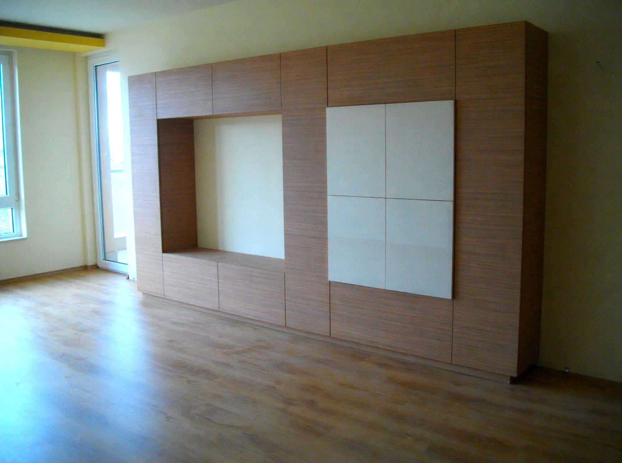 Ъглова модерна кухня по поръчка със светли гланцови шкафове, плот светъл дъб, черни дръжки и LED осветление.