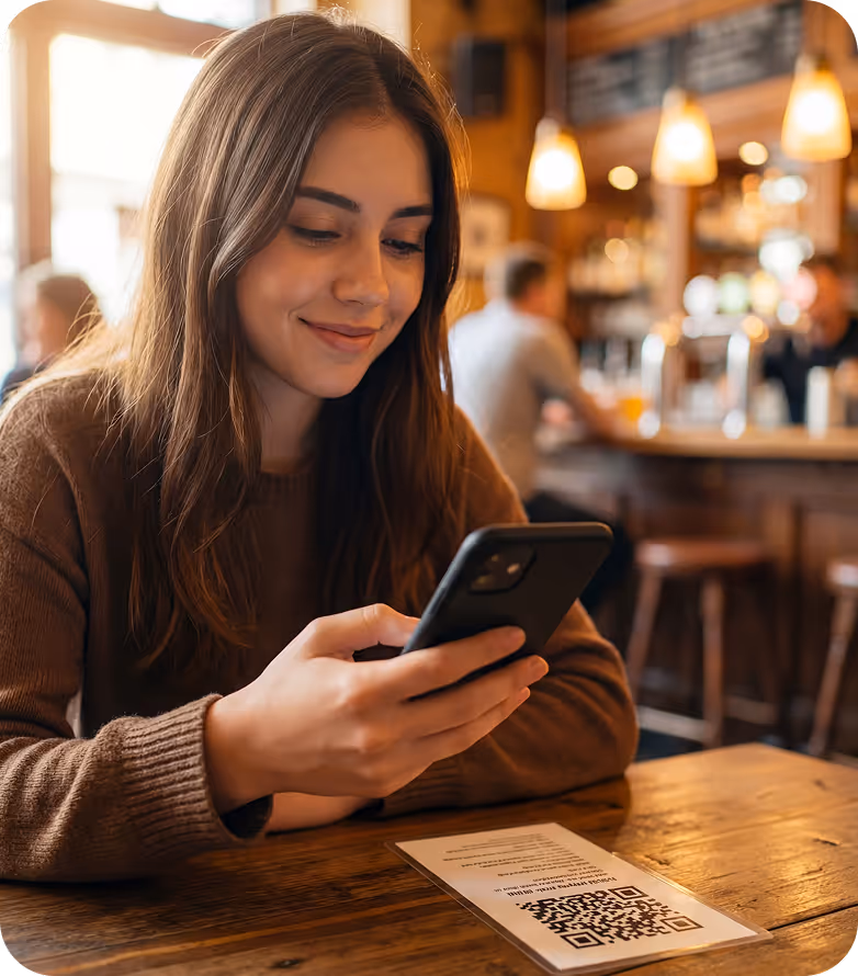 Junge Frau sitzt in einem Café und scannt mit ihrem Smartphone einen QR-Code auf dem Tisch.