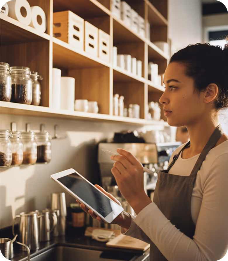 Eine Frau in Schürze bedient ein Tablet in einer modernen, gut organisierten Kaffeeküche.